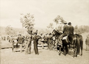 Men at an Australian sheep station. A large group of men, two on horseback, crowd around a wooden