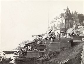 Ghats at Benares . Religious pilgrims sit beneath large umbrellas at a ghat (stepped wharf) on the
