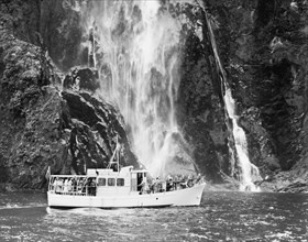 A tourist launch at Milford Sound. A launch carrying tourists cruises past a waterfall at Milford