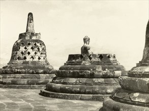 Statues of the Buddha at Borobudur. Bell-shaped stupas at the ninth century Buddhist monument of