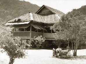 A weekend residence on Pangkor Island. Two European men relax in chairs outside a stilted bungalow