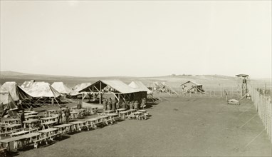 Mess tent at a British Army camp. Rows of tables are lined up outside the mess tent of a British