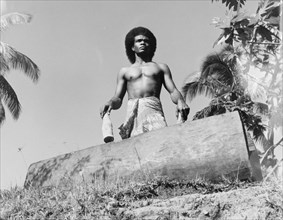 A Fijian drummer with a 'lali'. A Fijian man wearing a 'sulu' (wraparound skirt) stands over a
