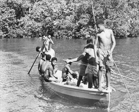 Boys in a canoe, Fiji. A group of boys in shorts relax in the sun as they pilot a canoe along a