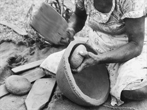 Making a clay pot, Fiji. A kneeling woman shapes a clay pot using a rounded stone and a wooden