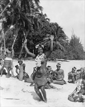 Performers on Moorea Island. A woman holds her hands in the air as she dances on a beach, dressed