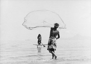 Fishing with a cast net. A Tahitian man wearing a printed 'pareu' (sarong) hurls a cast net into