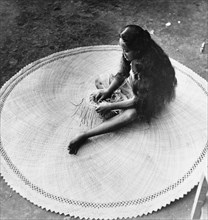 Weaving a mat from pandunas leaves . A Tahitian woman concentrates as she puts the finishing