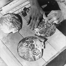 Seashells for the tourist trade. A craftsman uses a pointed tool to carve designs onto seashells