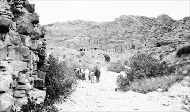 In the valley below Petra. Arab guides lead a European couple on horseback as they visit the cliff