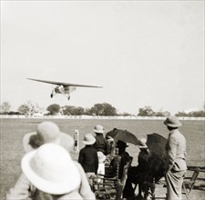 Flight over Moradabad'. A handful of spectators shield themselves from the sun with umbrellas as