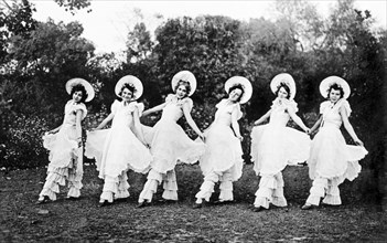 Chorus line act at a garden party. Members of the cast of 'Flying Fragments' in hoop skirts,