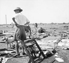 Storm damage at an Indian Police camp. George Boon stands with his hands on his hips as he surveys