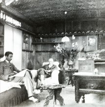 Reading the papers inside a shikara. Two men sit in armchairs, reading newspapers in the panelled