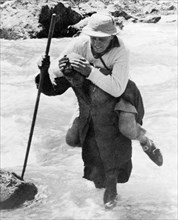 Crossing a Kashmiri Stream'. A Kashmiri trek porter carries a George Boon on his back as he