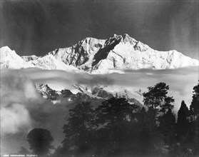 Kanchenjunga, circa 1919. The snow-capped peaks of Kanchenjunga mountain rise up above a layer of