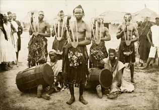 Nigerian musicians and hoe dancers. Five Nigerian hoe dancers, dressed in grass skirts with bells