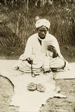 Nigerian man praying. A Nigerian man sits cross-legged on a mat, holding prayer beads in one hand