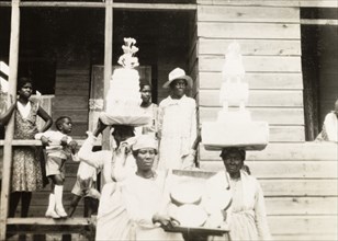 Wedding cakes in Trinidad. Two Trinidadian women balance tiered wedding cakes on their heads as