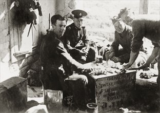 Army and police share a meal, Palestine. British military and police officers sit on oil cans