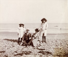 The Murray family on the beach. James and Minnie Murray sit on a shingle beach as they pose for a