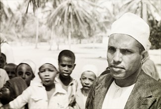 A Surahi type'. A Muslim man (possibly a teacher) stands in front of a group of children, staring
