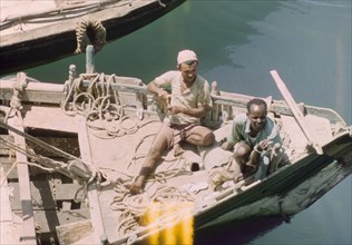 Traders in Aden harbour. Two traders relax in the sun on the deck of a dhow in Aden harbour. April
