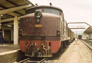 The train pauses for an hour'. A Uganda Railways locomotive waits in a station, pausing for a rest