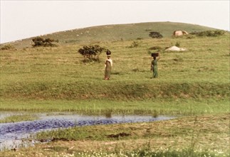 Two women collecting water. Two women balance containers on their heads as they collect water from