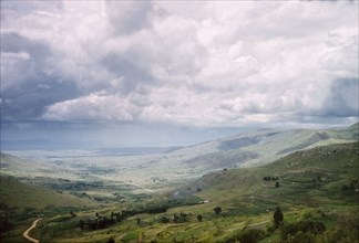 A view across Ankole. Rolling clouds hang over an extensive valley in Ankole. Terraced shambas can