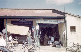 Dukas in Kampala bazaar. A duka (shop) selling clocks and a bicycle repairer in Kampala Road.