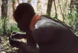 Rescuing a broken necklace. A Karamojong porter working with a British forestry survey team rescues