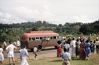 The faithful'. Crowds of people wave to a bus on a rural road during celebrations for the return
