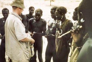Tobacco exchanged for news. British Game Ranger John Blower offers tobacco to a group of Toposa men