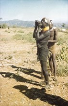 Lotuke with binoculars. Lotuke, a Suk porter working with a British forestry survey team, peers