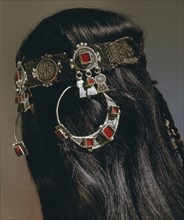 A silver headband from which hang large circular earrings inlaid with glass