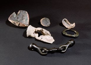 Left to right: triangular crucible used for melting bronze, two moulds, one for making a horses bit (also shown), a terret (guiding ring) and above that a fragment of a mould used for casting a decora...
