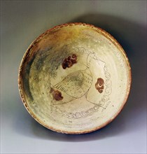 A redware pottery bowl with a design of a stork like bird scratched through the white slip before glazing