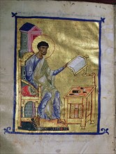 An illumination from a manuscript depicting St Luke seated before a table on which there appears to be engravers tools