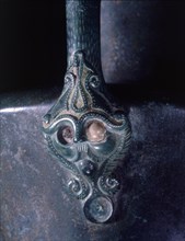Lower handle attachment of a bronze jug represents a bearded and moustached head which is crowned with an emblematic representation of the Tree of Life