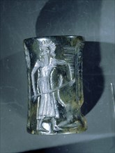 Akkadian cylinder seal inscribed with a scene of a seated deity wearing horned headdress, with attendant and a recumbent bull supporting a winged gate