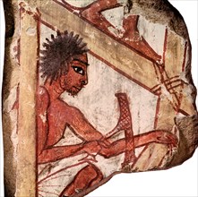 Painted relief fragment depicts a carpenter squatting on a scaffolding and working on a wooden object with his adze