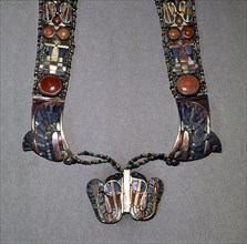 The counterpoise of a scarab pectoral from the tomb of Tutankhamun with straps formed from inlaid plaques with uraei (cobras), scarabs & solar discs