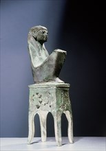 Seated bronze figure of the goddess Maat, wearing a tripartite wig, seated on an openwork throne of adoring winged uraei and Hathor masks