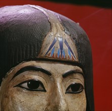 A mummy mask of a man with a heavy wig and an elaborate collar