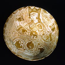 Lustreware plate with a design on an opaque white glaze of a seated figure holding drinking vessels