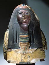 Upper part of an anthropomorphic coffin with blackened face, lotus ornamented wig, chest ornaments and a picture of the deceased kneeling to offer flowers to Osiris