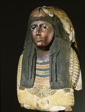 Upper part of an anthropomorphic coffin with blackened face, lotus ornamented wig, chest ornaments, and a picture of the deceased kneeling to offer flowers to Osiris