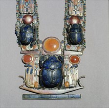 A scarab pectoral from the tomb of Tutankhamun with straps formed from inlaid plaques with uraei (cobras), scarabs & solar discs