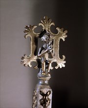 The top of a staff with a figure representing Christ on the Cross